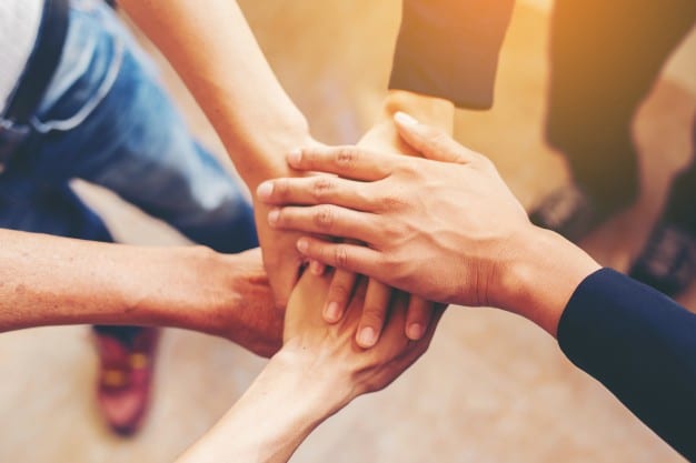 Multiple hands stacked together, symbolizing teamwork and unity.'