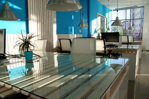 Office space featuring a glass table and walls with a touch of blue.