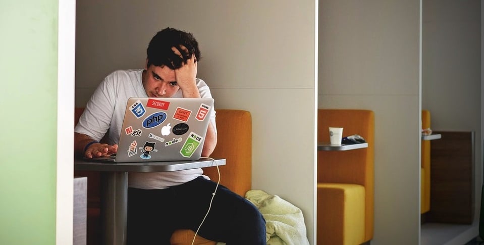 The man is seated, his expression focused as he looks at his laptop screen.
