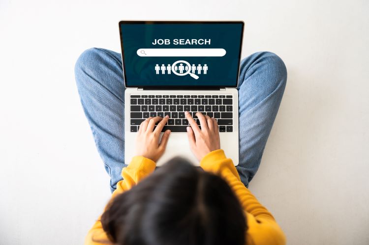 woman wearing a yellow shirt typing on her laptop