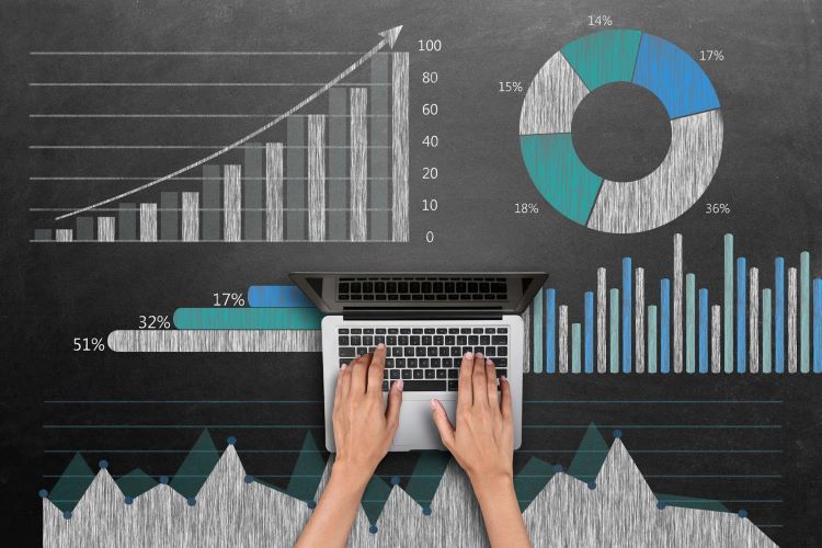 hands typing on laptop surrounded by charts and graphs