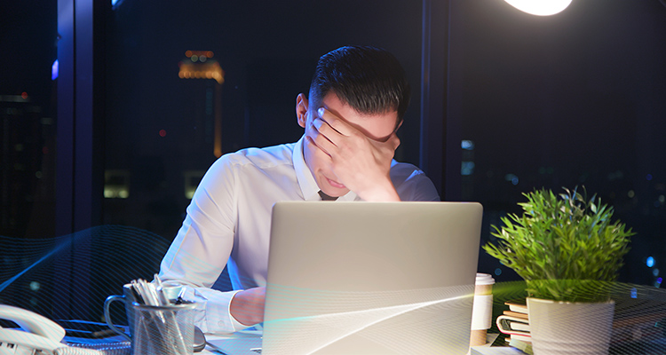 man covering his eyes with one hand and sitting in front of a computer