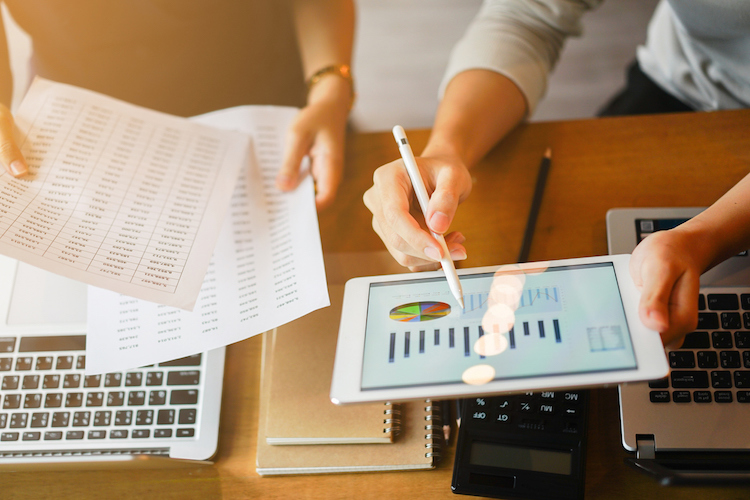 tablet showing graphs and charts and hands holding papers