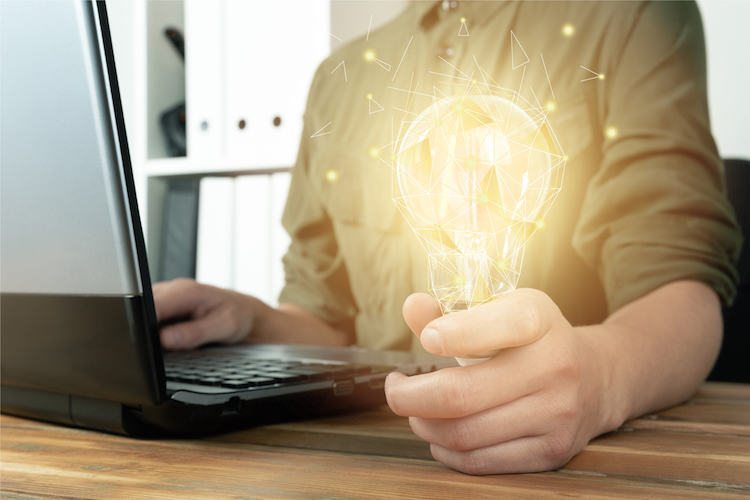 woman holding a lightbulb while sitting in front of a computer