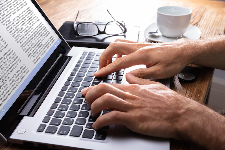 Person's Hand Typing On Laptop Over Wooden Desk