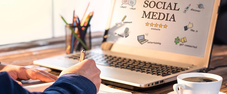 hand writing on notebook in front of a laptop with words social media on the screen