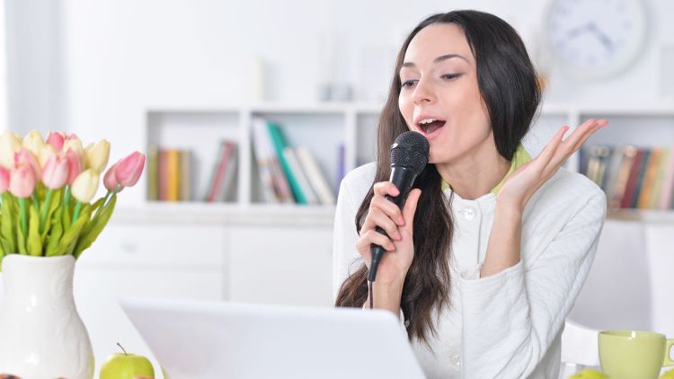 woman holding a microphone and singing in front of her laptop