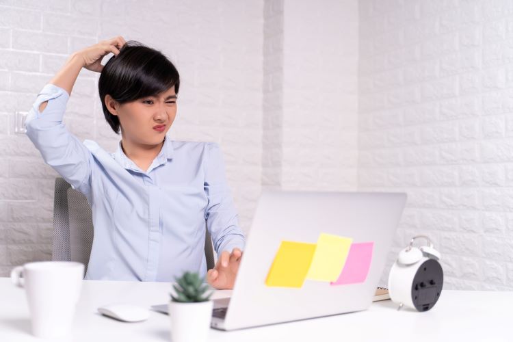 woman scratching her head while looking at her laptop screen