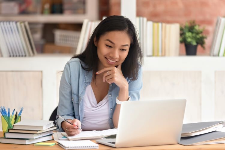 a woman taking notes while watching something on her laptop